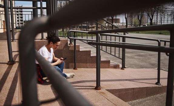 Young woman using mobile phone while sitting on skateboard on background of steps