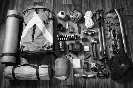 Equipment necessary for mountaineering and hiking on wooden background, black and white