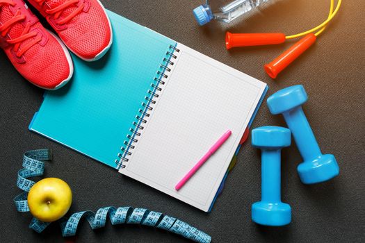 Notepad, a bottle of water, an apple, a skipping rope, dumbbells. Healthy diet, lifestyle concept of dumbbells, exercise, sport