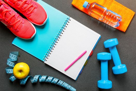 Notepad, a bottle of water, an apple, a skipping rope, dumbbells. Healthy diet, lifestyle concept of dumbbells, exercise, sport