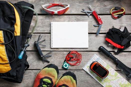 A set of accessories for cycling on a wooden background, With empty space and a notepad in the middle.