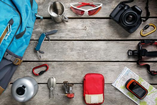 Tourist equipment for travel and tourism on a light wooden floor with an empty space in the middle. Card, knife, rope, carbine, flashlight, shoes, GPS, burner, mug, camera, glasses, backpack.