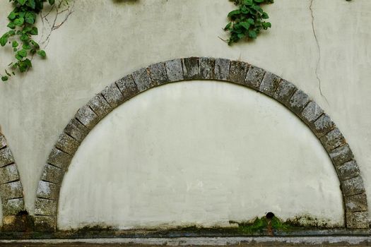 A walled door with a stone arch e against the background of an old beige plastered wall, photo frame, text place.