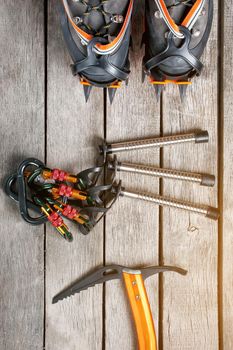 Top view of tourist equipment for a mountain trip on a rustic light wooden floor. Items include glasses, a card, a centipede, a carbine, an ice ax.