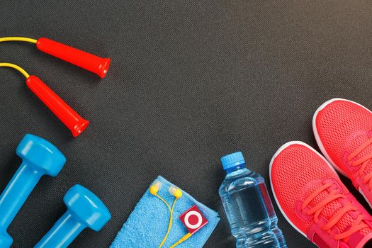 Top view of sports equipment, dumbbells, a skipping rope, a bottle of water, sneakers and a player. Against a gray background