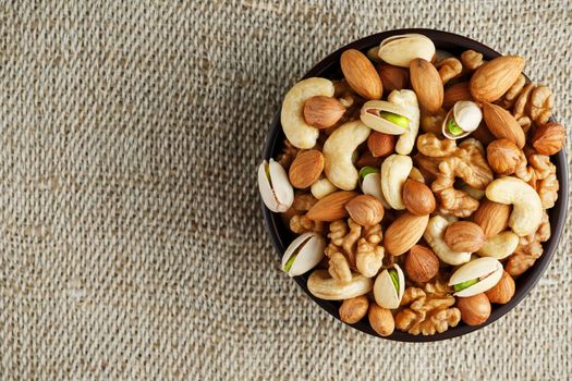 Mix of nuts of cashew, almonds, pistachios, hazelnuts and walnuts is against the background of brown fabric of burlap. Nuts as structure and background, macro