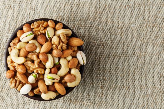 Mix of nuts of cashew, almonds, pistachios, hazelnuts and walnuts is against the background of brown fabric of burlap. Nuts as structure and background, macro