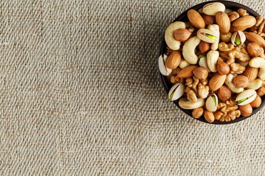 Mix of nuts of cashew, almonds, pistachios, hazelnuts and walnuts is against the background of brown fabric of burlap. Nuts as structure and background, macro