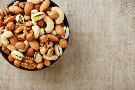 Mix of nuts of cashew, almonds, pistachios, hazelnuts and walnuts is against the background of brown fabric of burlap. Nuts as structure and background, macro