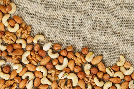 Mix of nuts of cashew, almonds, pistachios, hazelnuts and walnuts is against the background of brown fabric of burlap. Nuts as structure and background, macro