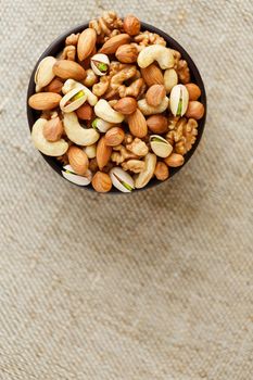 Mix of nuts of cashew, almonds, pistachios, hazelnuts and walnuts is against the background of brown fabric of burlap. Nuts as structure and background, macro