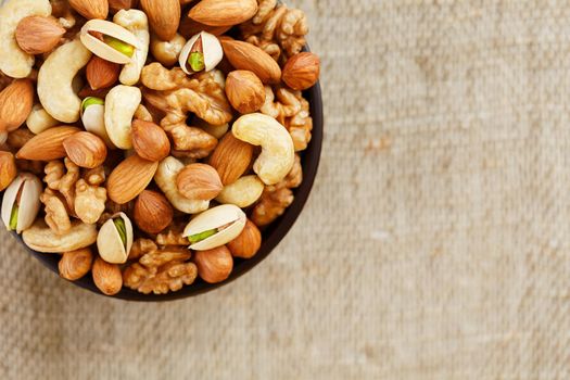 Mix of nuts of cashew, almonds, pistachios, hazelnuts and walnuts is against the background of brown fabric of burlap. Nuts as structure and background, macro