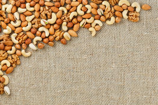 Mix of nuts of cashew, almonds, pistachios, hazelnuts and walnuts is against the background of brown fabric of burlap. Nuts as structure and background, macro