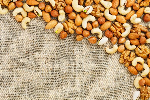 Mix of nuts of cashew, almonds, pistachios, hazelnuts and walnuts is against the background of brown fabric of burlap. Nuts as structure and background, macro