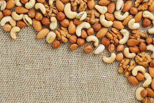 Mix of nuts of cashew, almonds, pistachios, hazelnuts and walnuts is against the background of brown fabric of burlap. Nuts as structure and background, macro