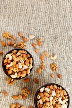 A mixture of cashew nuts, almond nuts, pistachios, hazelnuts and walnuts in a wooden cup against the background of burlap fabric. Nuts as structure and background, macro. Two cups of nuts.