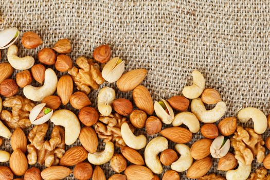 Mix of nuts of cashew, almonds, pistachios, hazelnuts and walnuts is against the background of brown fabric of burlap. Nuts as structure and background, macro