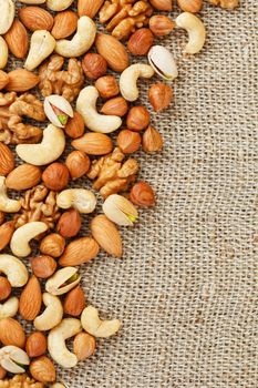 Mix of nuts of cashew, almonds, pistachios, hazelnuts and walnuts is against the background of brown fabric of burlap. Nuts as structure and background, macro