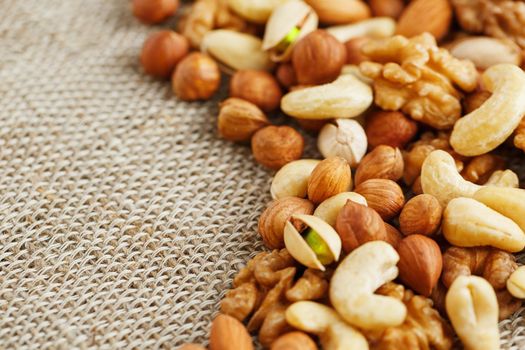 Mix of nuts of cashew, almonds, pistachios, hazelnuts and walnuts is against the background of brown fabric of burlap. Nuts as structure and background, macro