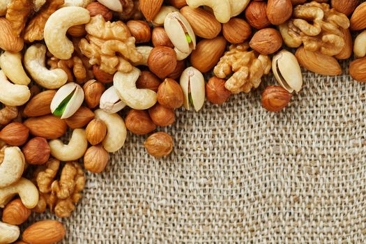 Mix of nuts of cashew, almonds, pistachios, hazelnuts and walnuts is against the background of brown fabric of burlap. Nuts as structure and background, macro