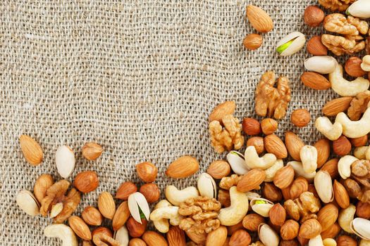 Mix of nuts of cashew, almonds, pistachios, hazelnuts and walnuts is against the background of brown fabric of burlap. Nuts as structure and background, macro