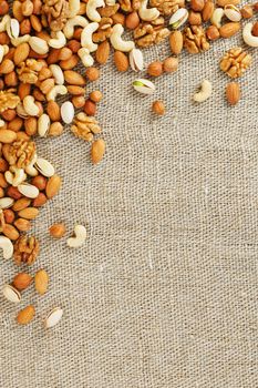 Mix of nuts of cashew, almonds, pistachios, hazelnuts and walnuts is against the background of brown fabric of burlap. Nuts as structure and background, macro