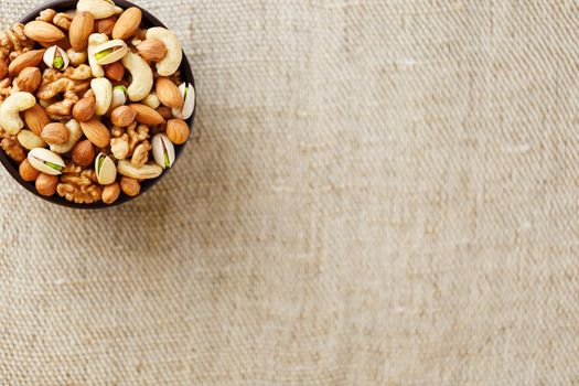 Mix of nuts of cashew, almonds, pistachios, hazelnuts and walnuts is against the background of brown fabric of burlap. Nuts as structure and background, macro