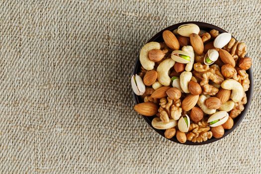 Mix of nuts of cashew, almonds, pistachios, hazelnuts and walnuts is against the background of brown fabric of burlap. Nuts as structure and background, macro