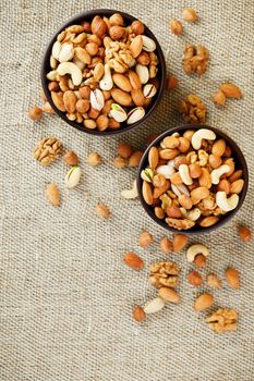 A mixture of cashew nuts, almond nuts, pistachios, hazelnuts and walnuts in a wooden cup against the background of burlap fabric. Nuts as structure and background, macro. Two cups of nuts.