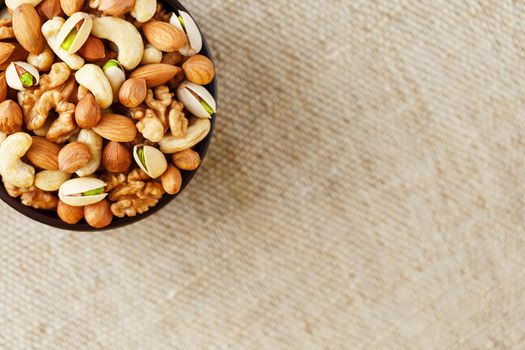 Mix of nuts of cashew, almonds, pistachios, hazelnuts and walnuts is against the background of brown fabric of burlap. Nuts as structure and background, macro