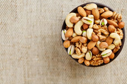 Mix of nuts of cashew, almonds, pistachios, hazelnuts and walnuts is against the background of brown fabric of burlap. Nuts as structure and background, macro