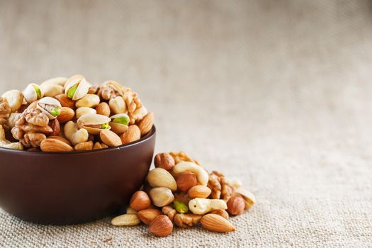 Mix of nuts of cashew, almonds, pistachios, hazelnuts and walnuts is against the background of brown fabric of burlap. Nuts as structure and background, macro