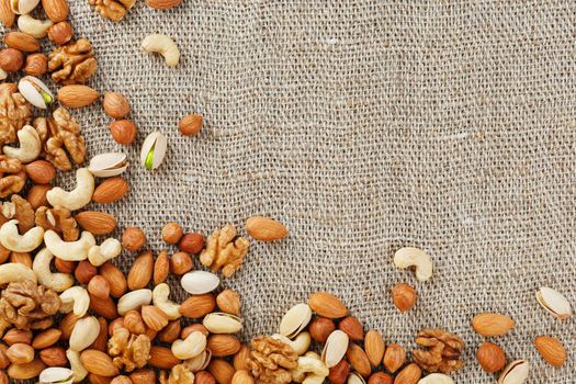 Mix of nuts of cashew, almonds, pistachios, hazelnuts and walnuts is against the background of brown fabric of burlap. Nuts as structure and background, macro