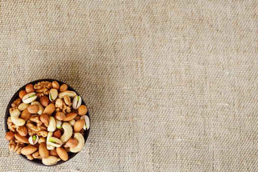 Mix of nuts of cashew, almonds, pistachios, hazelnuts and walnuts is against the background of brown fabric of burlap. Nuts as structure and background, macro