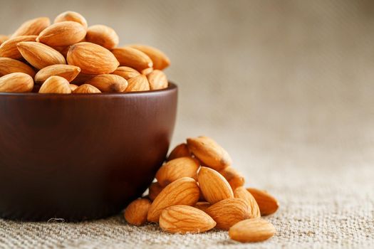 Almonds in a wooden cup on a burlap cloth background. Golden almond closeup in dark brown cup