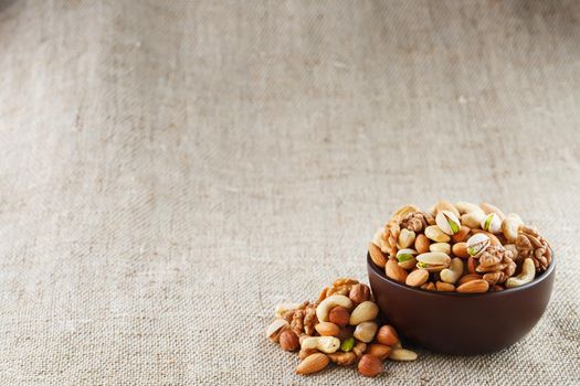 Mix of nuts of cashew, almonds, pistachios, hazelnuts and walnuts is against the background of brown fabric of burlap. Nuts as structure and background, macro