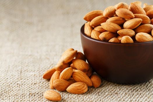 Almonds in a wooden cup on a burlap cloth background. Golden almond closeup in dark brown cup