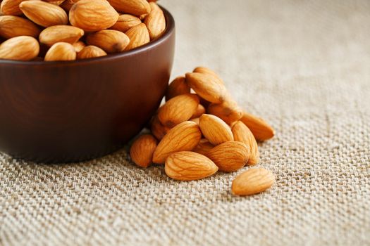 Almonds in a wooden cup on a burlap cloth background. Golden almond closeup in dark brown cup