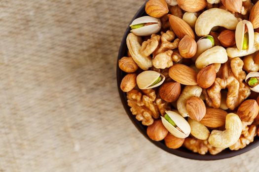 Mix of nuts of cashew, almonds, pistachios, hazelnuts and walnuts is against the background of brown fabric of burlap. Nuts as structure and background, macro