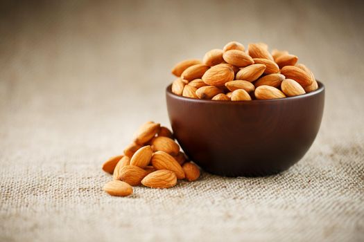 Almonds in a wooden cup on a burlap cloth background. Golden almond closeup in dark brown cup