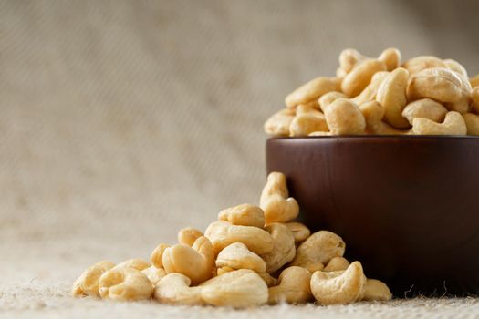 Cashew nuts in a wooden bowl on a burlap cloth background. Golden cashew close-up in a dark brown cup.