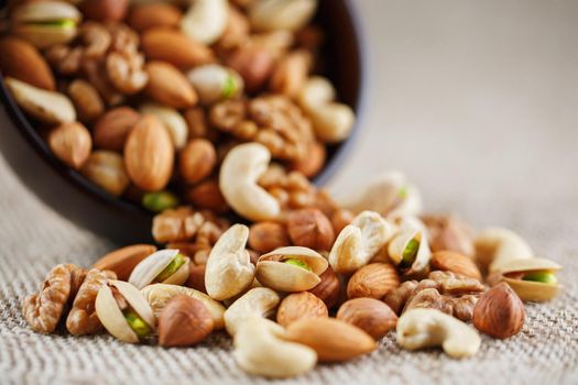 Mix of Dish of walnut, hazelnuts, almond, ketob and pistachios spilled from a cup on the background of cloth from burlap. Nuts as structure and background, macro.