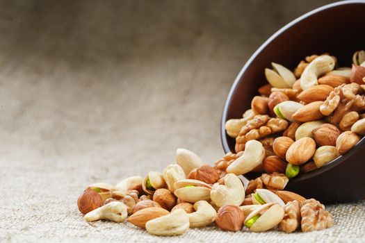 Mix of Dish of walnut, hazelnuts, almond, ketob and pistachios spilled from a cup on the background of cloth from burlap. Nuts as structure and background, macro.