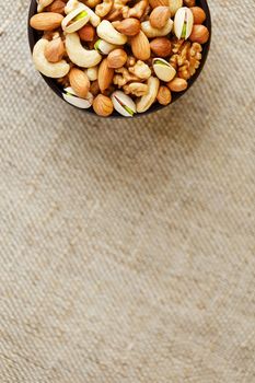 Mix of nuts of cashew, almonds, pistachios, hazelnuts and walnuts is against the background of brown fabric of burlap. Nuts as structure and background, macro