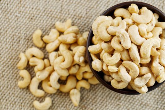 Cashew nuts in a wooden bowl on a burlap cloth background. Golden cashew close-up in a dark brown cup.