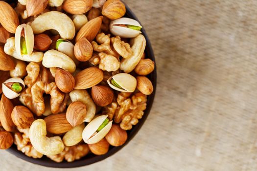 Mix of nuts of cashew, almonds, pistachios, hazelnuts and walnuts is against the background of brown fabric of burlap. Nuts as structure and background, macro