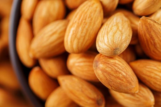 Almonds in a wooden cup on a burlap cloth background. Golden almond closeup in dark brown cup