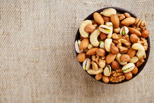 Mix of nuts of cashew, almonds, pistachios, hazelnuts and walnuts is against the background of brown fabric of burlap. Nuts as structure and background, macro