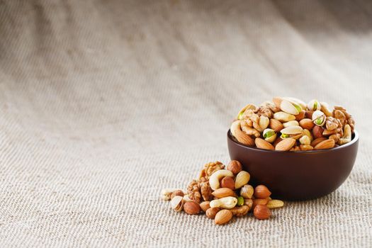 Mix of nuts of cashew, almonds, pistachios, hazelnuts and walnuts is against the background of brown fabric of burlap. Nuts as structure and background, macro