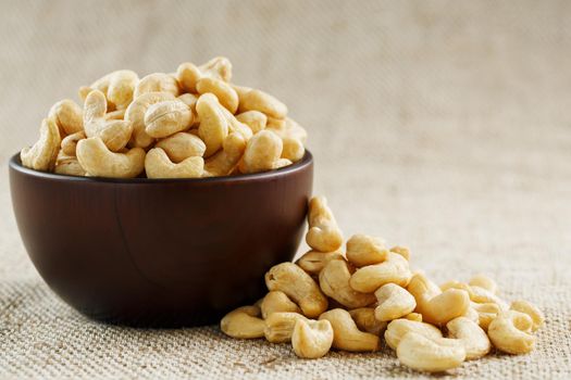 Cashew nuts in a wooden bowl on a burlap cloth background. Golden cashew close-up in a dark brown cup.